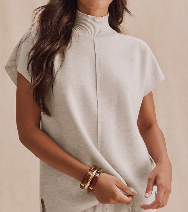 Model in cream colored turtleneck short sleeve top against cream colored background